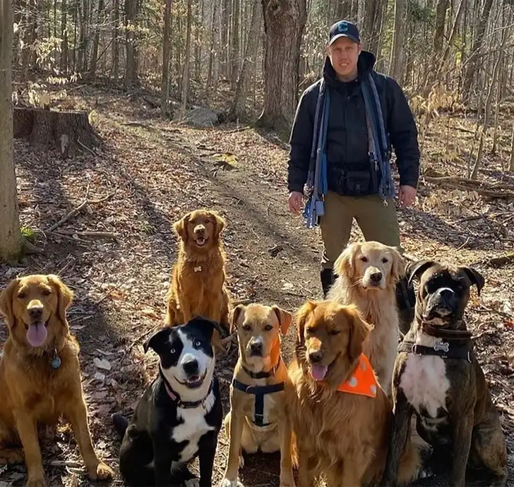 Ryan standing on a woodland trail behind a seated group of nine dogs