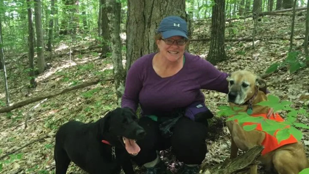 Sara kneeling in the woods with two of her dogs