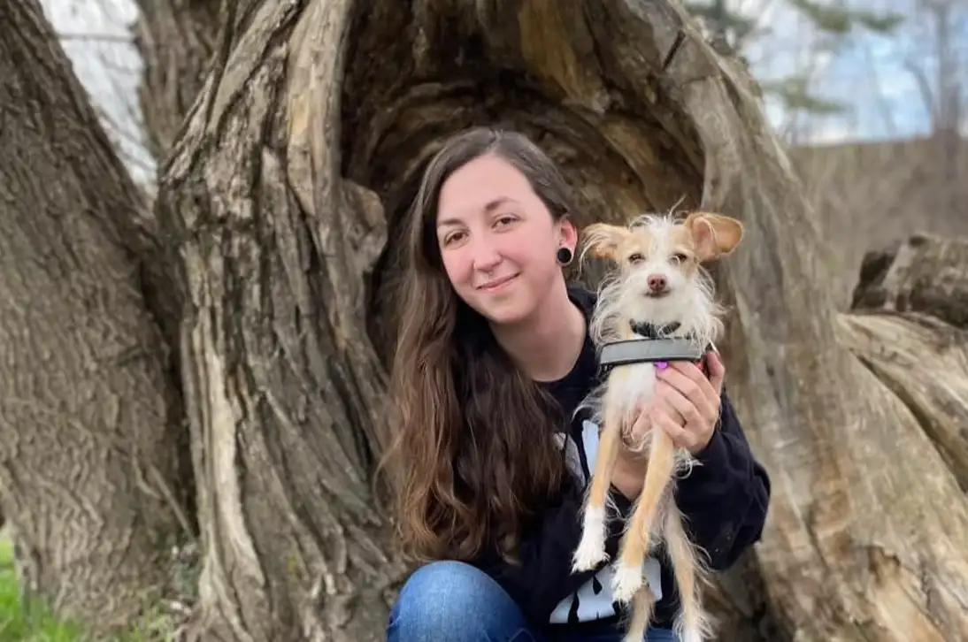 Tasha kneeling by a hollow tree holding her small scruffy dog