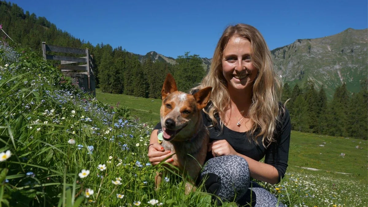 Valerie kneeling in an alpine meadow with her red heeler